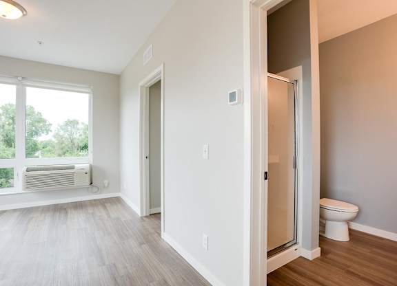 View looking into bathroom with standup shower and toilet and living room with large window