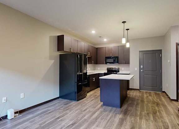 an open-concept living room and kitchen with dark cabinets and black appliances