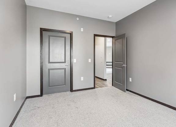 Carpeted apartment bedroom with gray walls, double-door closet access, and an open doorway leading to the hallway.