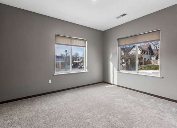 Spacious apartment bedroom with soft carpeting, two large windows, and abundant natural light.