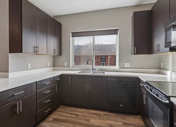 Contemporary apartment kitchen with dark wood cabinetry, quartz-style countertops, a large window, and an L-shaped layout.