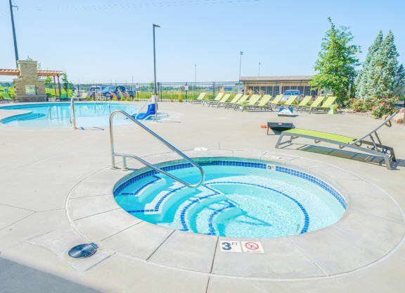 a hot tub with green lounge chairs and trees in the background