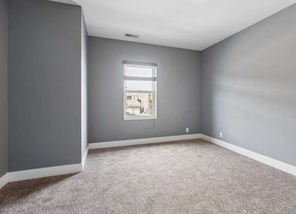 Soft natural light enters this unfurnished apartment bedroom, highlighting gray walls, neutral carpeting, and crisp white trim.