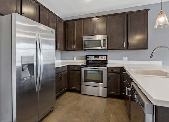 Dark wood cabinetry wraps around this apartment kitchen, paired with white counters, stainless steel appliances, and a peninsula sink.
