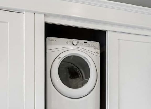 Stacked washer and dryer fit neatly into a recessed apartment laundry closet with white sliding doors and trim.