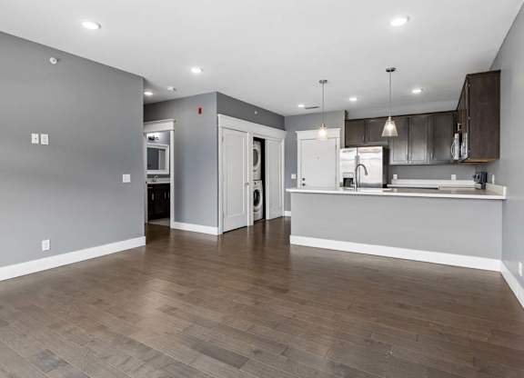 Open apartment living area leads into a kitchen with dark cabinetry, a breakfast bar, pendant lighting, and nearby in-home laundry.