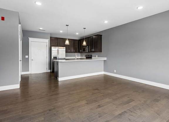Generous living area with wood-look flooring opens to a dark-cabinet kitchen, breakfast bar, and stainless steel appliances.