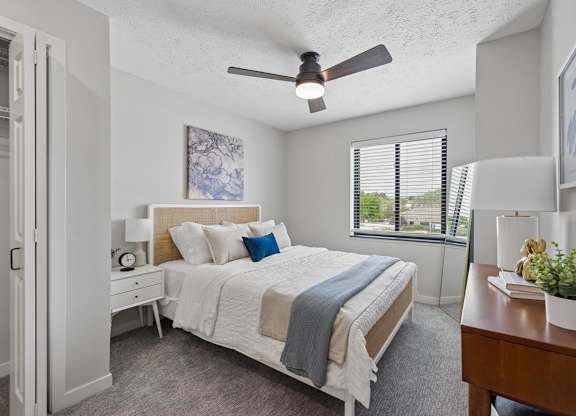 Bright apartment bedroom with ceiling fan and large window.
