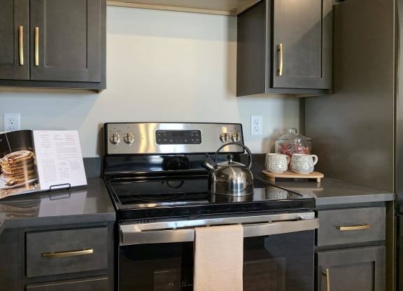 a kitchen with black cabinets with gold handles and stainless steel stove
