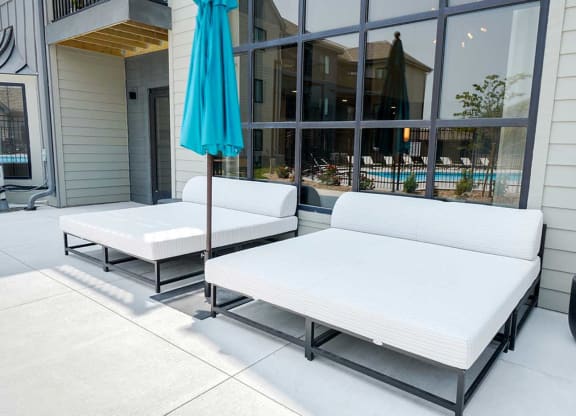a patio space in front of a large window with two outdoor daybeds and an umbrella