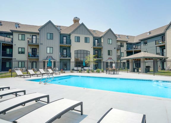 a swimming pool in the center of an apartment courtyard with lounge chairs next to it