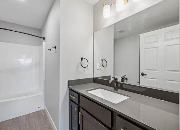 Apartment bathroom with a single-sink vanity, dark cabinetry, a large framed mirror, and a tub-shower combination with a white surround.