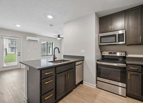 Modern apartment kitchen with dark cabinetry, stainless steel appliances, a center island with storage, and an open layout connected to the living area.