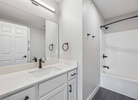 Apartment bathroom with white vanity, black fixtures, and tub-shower combination with surround.