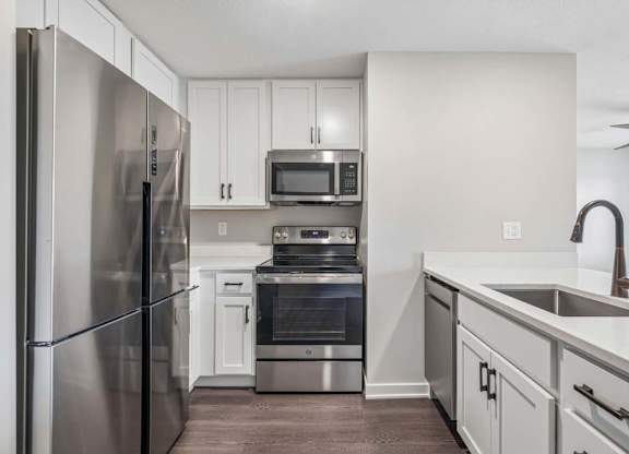 Apartment kitchen with white cabinetry, stainless steel appliances, and oversized peninsula with built-in sink.
