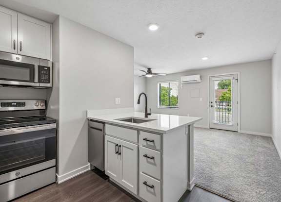 Open apartment living area with kitchen island, stainless steel appliances, and private balcony access.