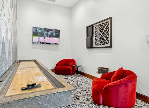 A room with a shuffleboard table and red chairs.