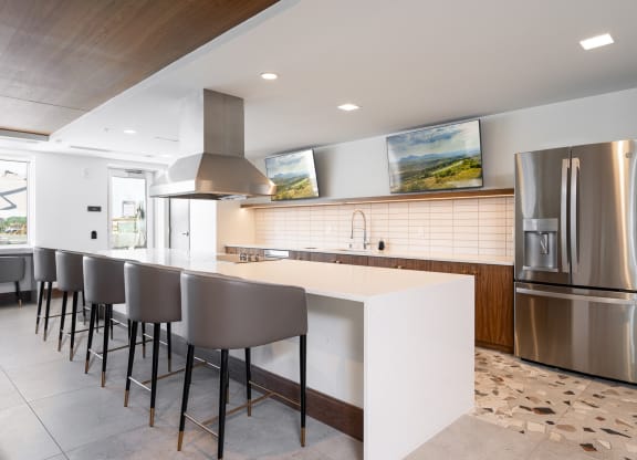 Community space kitchen with full stove, fridge, and oven. Large white countertop with barstool seating.