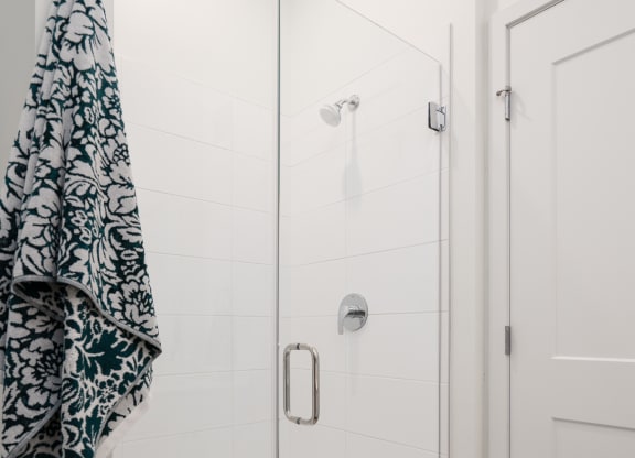 Walk in shower with glass door and towel hanging on rack to the right