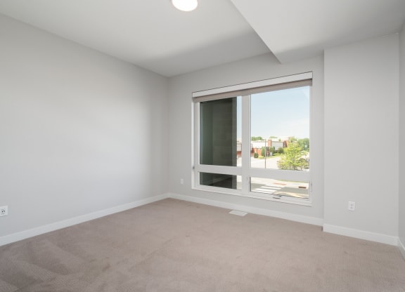 Second bedroom with large floor to ceiling window, beige carpet, and white walls.
