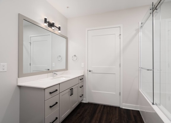beautiful white bathroom with grey vanity and large mirror with glass shower doors