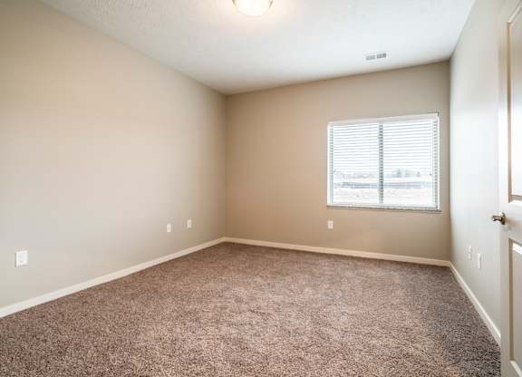A bedroom with a carpeted floor and a window with blinds.