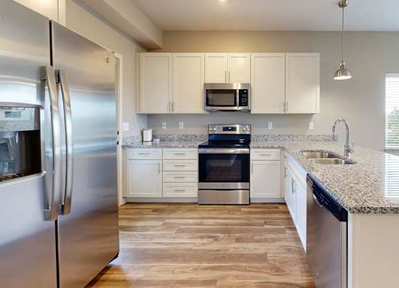 A modern kitchen with stainless steel appliances and wooden flooring.
