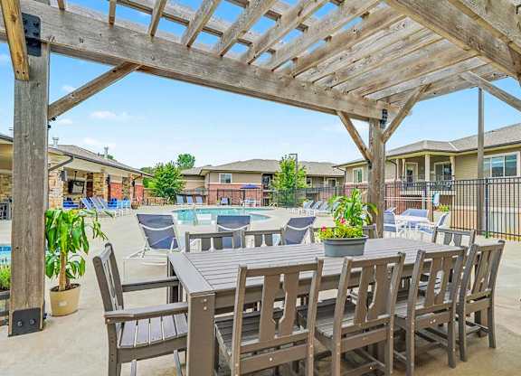A wooden pergola over a table with chairs and potted plants.