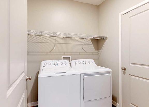 A full-sized washer and dryer in a laundry room, with overhead shelving.