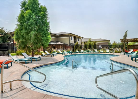 Organically shaped resort style pool surrounded a pool deck with bright blue lounge chairs