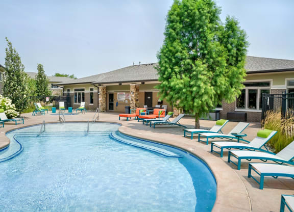 Organically shaped resort style pool surrounded a pool deck with bright blue lounge chairs
