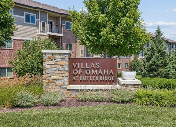 Villas of Omaha at Butler Ridge apartment community entrance sign surrounded by landscaped greenery and residential buildings.