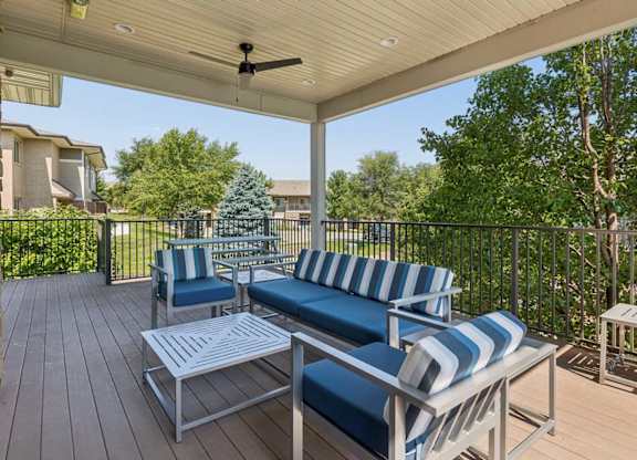Covered outdoor lounge at Villas of Omaha at Butler Ridge with blue cushioned seating, tables, ceiling fan, and community views.