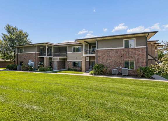 Apartment exterior with brick siding, private balconies, green lawn, and mature landscaping.
