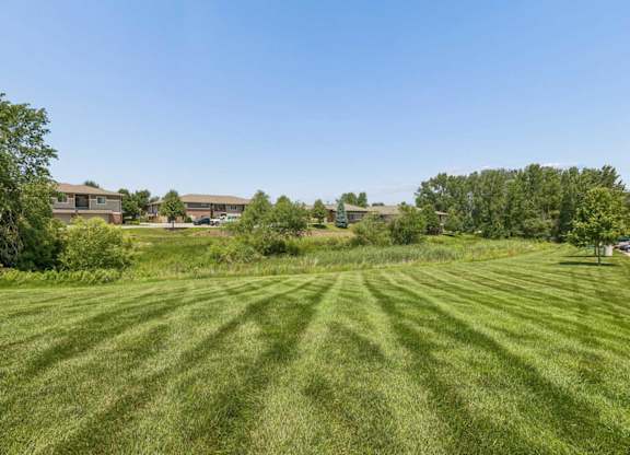 Expansive green lawn and natural landscaping at Villas of Omaha at Butler Ridge, with apartment buildings and mature trees beyond.