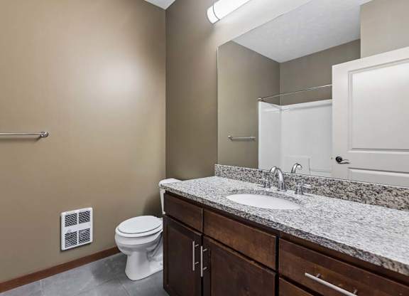 Apartment bathroom with a granite-look vanity, dark wood cabinetry, large mirror, neutral walls, and a tub-shower combination