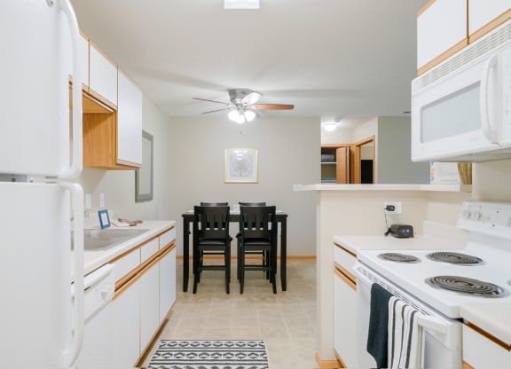 a kitchen with white appliances and a dining room table with chairs in the back