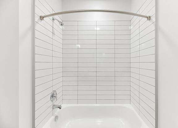 A white tiled bathroom with a white tub and a white shower curtain.