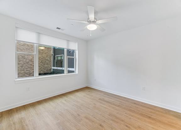A room with a ceiling fan and a window overlooking a building.