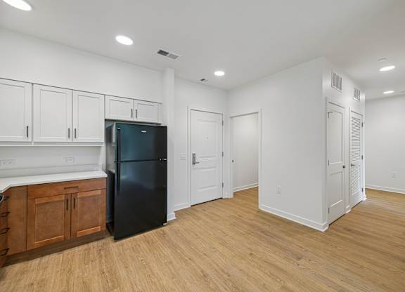 A black refrigerator sits in a kitchen with wooden floors and white walls.