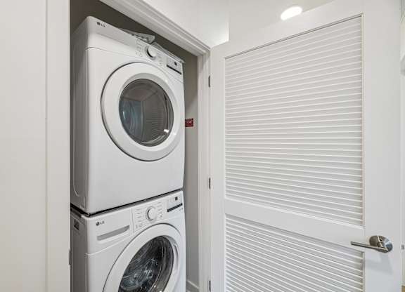 A white washing machine is stacked on top of another in a small laundry room.