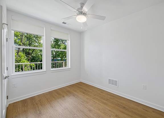 A room with a ceiling fan and a window overlooking a balcony.