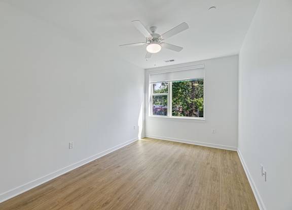 A room with a ceiling fan and a window with a view of trees.