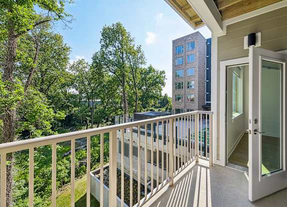 A balcony with a glass door leading to a room with a view of a tree-filled area.