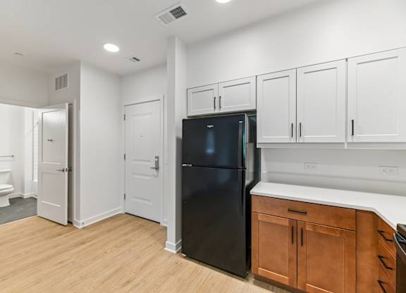 A black refrigerator is in a kitchen with white cabinets and a wooden floor.