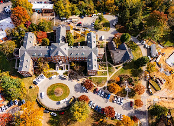 An aerial view of a campus with a large building in the center and a parking lot with cars.