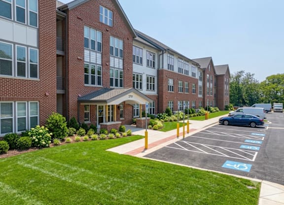 A parking lot in front of a brick building with a car parked in the spot with a handicap sign.