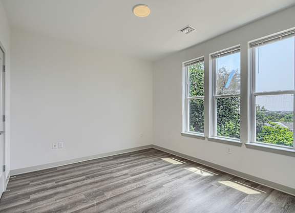 A room with a white door, a window, and a wooden floor.