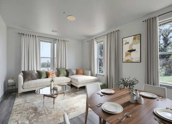 A dining room with a table set for two and a couch with pillows.