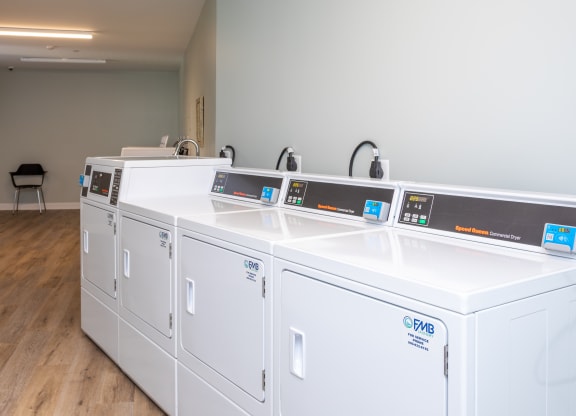 four washers and dryers in a row in a room with wood flooring